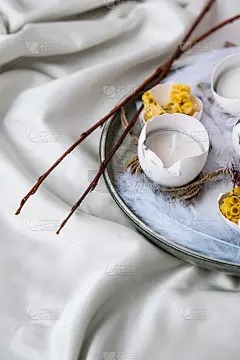 时髦的复活节装饰品。打碎的有机鸡蛋与干草和干花在盘子里。蜡烛在白色的蛋壳。鸟的羽毛。副本的空间。贺卡