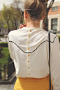 Long sleeve back-button-down blouse with black western piping. Paired with a mustard leather skirt and black cat-eyed sunglasses.