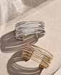 David Yurman cuffs in sterling silver with pavé diamonds or in 18K yellow gold with pavé diamonds on a light pink stone surface with long shadows. 