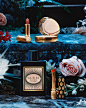 Stone steps in a garden appear lit with blue moonlight and a selection of Gucci Beauty products lay strewn among flowers on the steps. Central to the image is the Gucci Bloom Eau de Parfum Intense bottle which is encased in a black bottle with a peach, bl