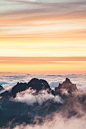 Jagged mountain peaks emerge from a sea of clouds during sunset