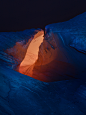 This may contain: an orange light shines in the middle of a blue rock formation with snow on it