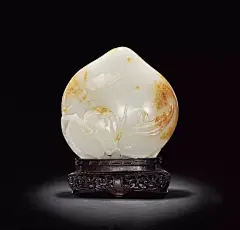 清乾隆
白玉寿桃摆件
H: 12cm
摆件取整块白玉随形雕琢而成，体量硕大，玉质温润，色泽晶莹，纯洁细腻。寿桃下部随玉形雕出枝叶，枝苍劲嶙峋，叶舒展灵动，栩栩如生。《神农本草》中记载“玉桃服之，长生不死”，因此桃被称为寿桃，成为祝福的代表物，而玉雕寿桃尤以为贵。玉桃上有双翅大展的蝙蝠，似为桃实的鲜美所吸引，不期而至，动感十足。器物以整玉圆雕成寿桃与蝙蝠，代表“福寿”之意，此寿桃集阴刻、浮雕于一器，技法娴熟，构思精致。寿桃似饱满多汁，叶子脉络清晰，线条流畅，寥寥数刀之间深显雕刻者之匠心独运及高超技法；其上枝