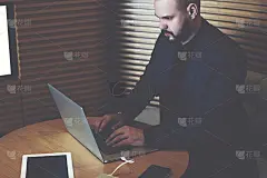 一位年轻的总经理正通过一台笔记本电脑在互联网上写一则寻找金融专家的广告，而他正坐在办公室内部的屏幕旁