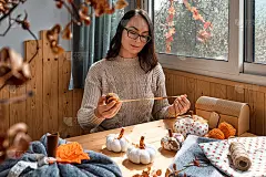 舒适的南瓜。一位妇女正在制作彩色织物南瓜。木桌上的手工南瓜装饰。共鸣。感恩节装饰。