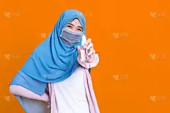 在病毒爆发时，穿着传统服装的亚洲穆斯林妇女戴着医用口罩，用分离的彩色背景酒精凝胶洗手