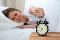 昏昏欲睡的年轻女子伸出手来敲响警钟，愿意关掉它。早醒、睡眠不足的概念