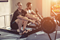 Side view of man and woman doing exercises with rowing machine at gym.