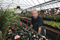 A man standing in a greenhouse with shelves of plants.  by Mint Images on 500px