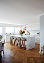 Design ideas for a large transitional open plan kitchen in Sydney with a farmhouse sink, recessed-panel cabinets, white cabinets, quartz benchtops, white splashback, ceramic splashback, black appliances, medium hardwood floors, with island, brown floor an