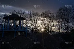 光秃秃的树枝和夕阳下的花园房子。黑暗的夜晚。