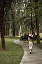 woman in brown long sleeve shirt and brown skirt walking on pathway between green grass and