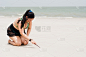 怀孕成熟的女人跪在沙滩上，在白沙地上写字或画画
