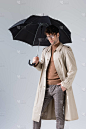 自信、时髦的男人站在伞下，手插在灰色的口袋里