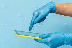 一只戴着医用手套的女性手拿着一个蓝色背景上的空白现代平板电脑。模拟。