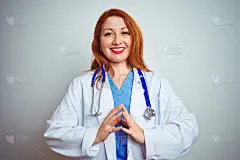 年轻的红发女医生在白色孤立的背景下使用听诊器双手并拢，十指交叉，微笑轻松和愉快。成功和乐观