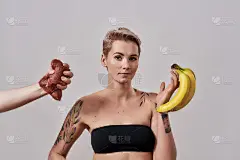 我选择水果。迷人的刺鼻纹身女子拒绝吃别人给她的肉，在灰色背景下选择孤立的香蕉