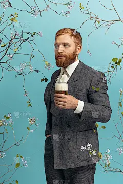 年轻的红发和胡子男子的肖像与一杯啤酒孤立在蓝色的花卉背景