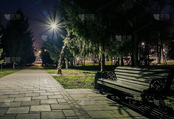 夜晚的城市公园。木凳、路灯和绿树。铺着瓦片的路在夜晚的公园里挂着灯笼。晚上在公园的长椅上。在晚上用灯