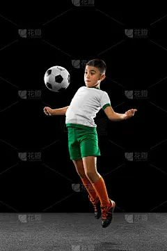 男孩的全身肖像，孩子，足球运动员在统一训练，踢球与胸部在一个跳跃孤立的黑色背景。