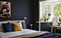 深蓝色卧室的一角，摆放着一张双人床，窗台上则放着花盆。