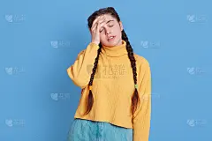 肖像烦可爱的女性穿着黄色毛衣做捂脸的手势，保持闭上眼睛，触摸额头在绝望和愤怒，被蓝色的墙心烦意乱。