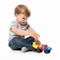 A child sits on the ground with one hand reaching forward to touch a toy on a white background