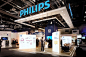 This may contain: people are standing in front of the phillips booth at an electronics show, which is open for business