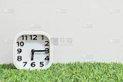 特写白色时钟装饰显示在6点15分或早上6点15分，绿色的人造草地板和奶油色壁纸纹理背景与复制空间