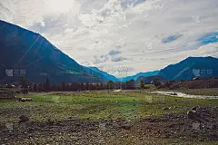 村谷。在阳光下的大山背景上的高地上的牲畜。在阳光下，羊群在山河附近吃草。壮丽的大自然令人惊叹的大气景