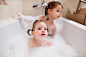 Two little girls having bath with bubbles in bathtub