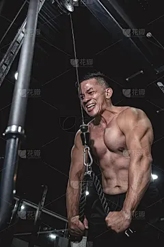 一名健康的亚洲男子在用力推钢丝绳。在健身房或健身俱乐部锻炼肱三头肌。低角度拍摄。