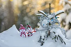 两个有趣的小玩具娃娃雪人在编织的帽子和围巾在深雪户外附近的松树树枝。新年快乐，并附上圣诞贺卡。