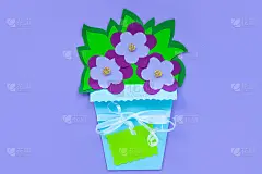 蓝色纸花与叶子在一个篮子在紫色的背景，贺卡标签模型。插花平铺