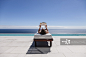 Woman reading on lounge chair at poolside overlooking ocean_创意图片