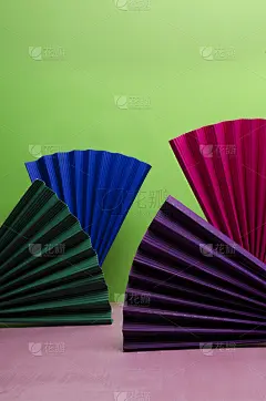 垂直的图像。不同颜色的纸扇在粉红色的表面上衬托绿色的背景。空的空间