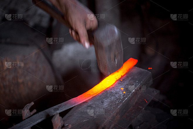 铁匠的手在工作。一只手拿着锤子，另一只手拿着铁质工件。师傅有条不紊地锤击铁砧。这是古代手工艺艰苦劳作