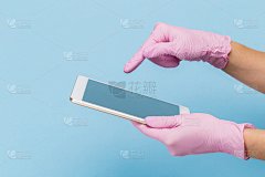 一只戴着粉色医用手套的女性手拿着一个蓝色背景上的空白现代平板电脑。模拟，名片