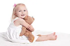Happy Little Girl in White Dress Hugging Stuffed Animal