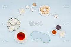 棉花睡眠面膜，自制饼干，一杯花草茶，干燥的薰衣草花和蓝色背景的蜡烛。俯视图，平放。