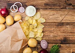 新鲜有机自制薯片配酸奶油、红洋葱和香料，装在纸袋里，木质背景。新鲜的黄土豆