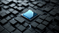 A black and white 3D rendering of an abstract square chip, with a blue glass panel on top, placed in the center of an intricate pattern made up entirely of tiny squares. The background is a dark gray color. This design creates a sense of depth and texture