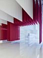 访客穿过形似中国红门的层层布幔进入展厅。展厅按照不同的功能，被划分为有着各自元素的展区，其他保留成休息区。在这一楼层，白色、轻质的稍透明幕布从开放式天花垂悬而下。布料的垂直性也把天花板的高度降低到参观者舒适的尺度，大量的白色织物显得沉稳大度，增加了展厅的仪式感，后方的“红色中国门”同时彰显一种帝王的雍容气质。