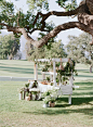 Ceremony Program Cart--As guests entered the alfresco ceremony space, they were welcomed by a white wooden flower cart that was topped with ceremony programs and adorned with potted plants and hanging herbs.