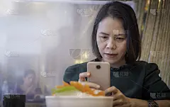 亚洲女性，泰国，黑头发，长相不错，在一家日本餐厅，用智能手机拍美食照片。智能手机上的摄像头是定制的，