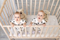 两个双胞胎宝宝的兄妹8个月大的时候穿着睡衣坐在婴儿床里，看着摄像机，俯瞰风景，友情的概念，文字的地方