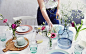 餐桌布置：淡彩色餐具，形状各异的玻璃花瓶插有鲜花，铺有纯棉桌布和木板。
