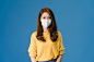 Young asia girl wearing medical face mask with dressed in casual clothing and looking at camera isolated on blue background. self-isolation, social distancing, quarantine for corona virus prevention. Free Photo