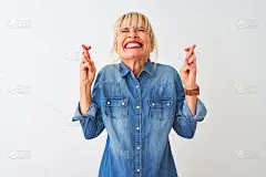 中年妇女穿着休闲牛仔衬衫站在孤立的白色背景手势交叉手指微笑希望和闭上眼睛。运气和迷信的概念。