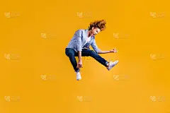 全身大小的照片疯狂红发摇滚小子音乐家粉丝穿着牛仔裤牛仔格子蓝衬衫运动鞋假装弹吉他跳跃孤立生动的色彩背